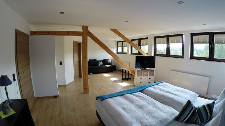 Ein helles und modernes Zimmer mit Holzbalken und großen Fenstern. Es gibt ein großes Bett, einen Fernseher und eine Couch.