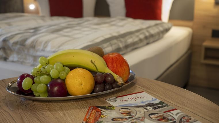 Ein frisches Obstarrangement auf einem Tisch neben einem bequemen Bett. Im Hintergrund sieht man gemütliche Bettwäsche und Kissen.