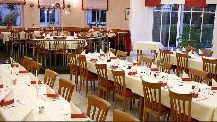 Une salle à manger élégante avec des tables dressées. Les tables sont décorées de nappes blanches et de serviettes rouges.