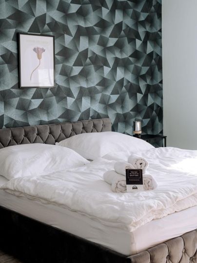 Ein stilvolles Schlafzimmer mit einem gepolsterten Bett und eleganter Bettwäsche. Die geometrische Tapete und das Kunstwerk verleihen dem Raum eine moderne Note.