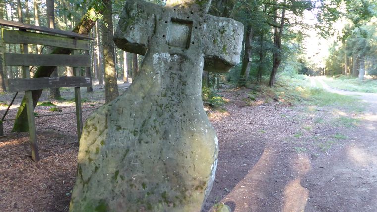 Croix de pierre dans la forêt, entourée d'arbres et d'un chemin.