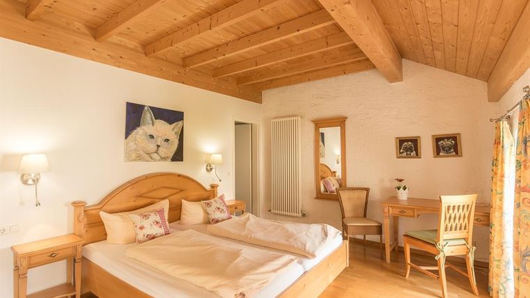 Une chambre confortable avec des plafonds en bois et un grand lit double. Des images sont accrochées aux murs, et il y a un petit espace de travail avec une chaise.