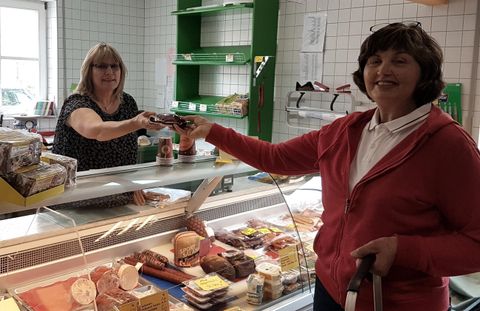 Une femme achète des aliments à un comptoir. En arrière-plan, une vendeuse se tient et lui tend un produit.