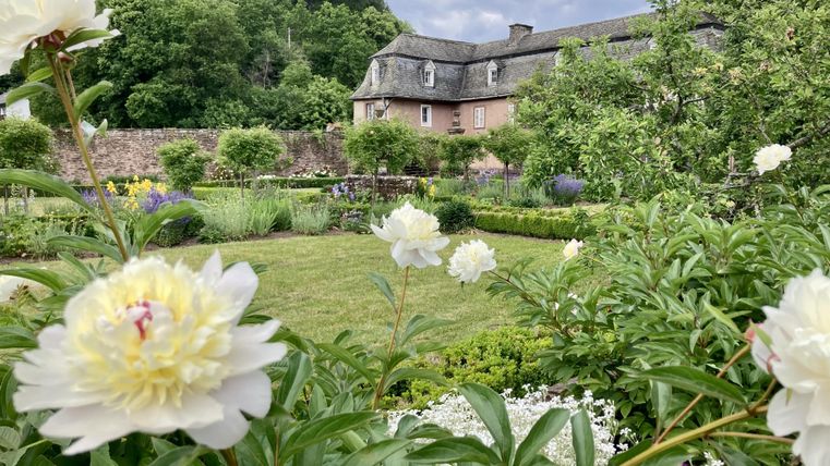 Ein schöner Garten mit blühenden weißen Pfingstrosen und einer sanften Rasenfläche. Im Hintergrund ist ein historisches Gebäude und üppiges Grün zu sehen.