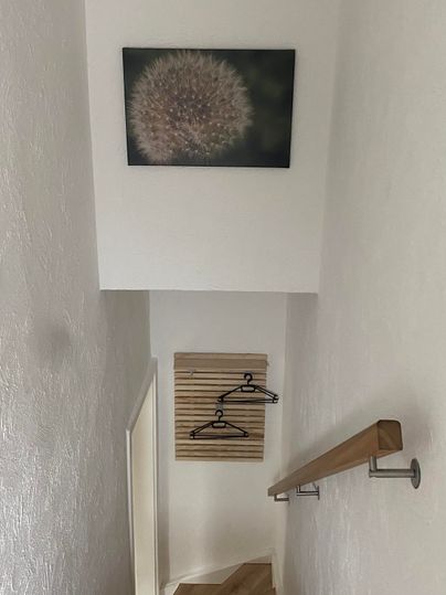 Eine Treppe mit hellen Wänden und Holzfußboden. An der Wand hängt ein Bild und eine Holzleiste mit Kleiderhaken.