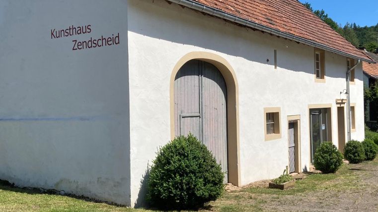 An art house with a white façade and a red roof. The entrance is decorated with a large wooden door and small bushes.