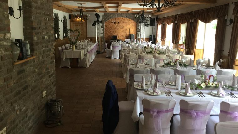 A festively decorated hall with long tables. The tables are adorned with white cloths and purple ribbons, ready for a celebration.
