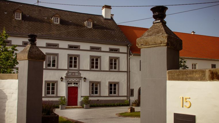 Een stijlvol gebouw met een rode deur en grote ramen. Het is omgeven door een muur met zuilen en heeft een uitnodigende ingang.