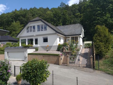A modern house with a beautiful garden and a driveway. Behind the house are trees that give the surroundings a green touch.