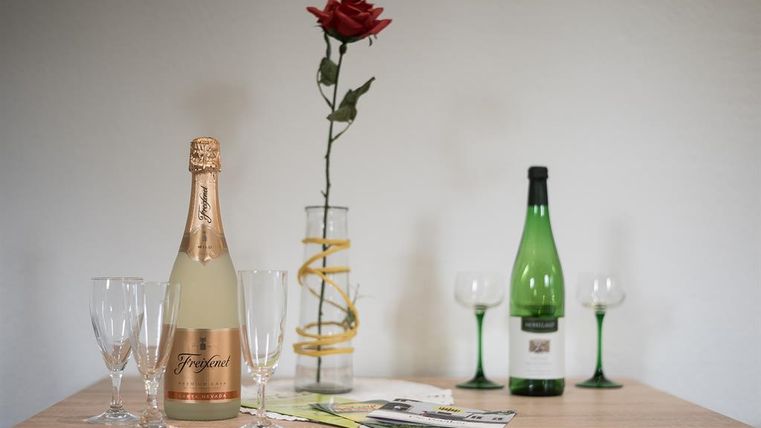 Une table avec des bouteilles de champagne, des oiseaux de vitrine et des verres. Au centre se trouve une rose dans un vase, entourée de prospectus.