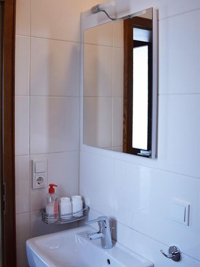 Une salle de bains moderne avec un lavabo et un miroir. Les murs sont carrelés en clair et il y a quelques articles de toilette sur une étagère.