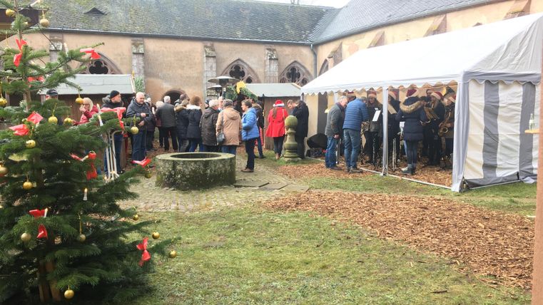 Eine festliche Veranstaltung im Freien mit einer großen Menschenmenge unter einem Zelt. Im Vordergrund steht ein Weihnachtsbaum mit roten Dekorationen.