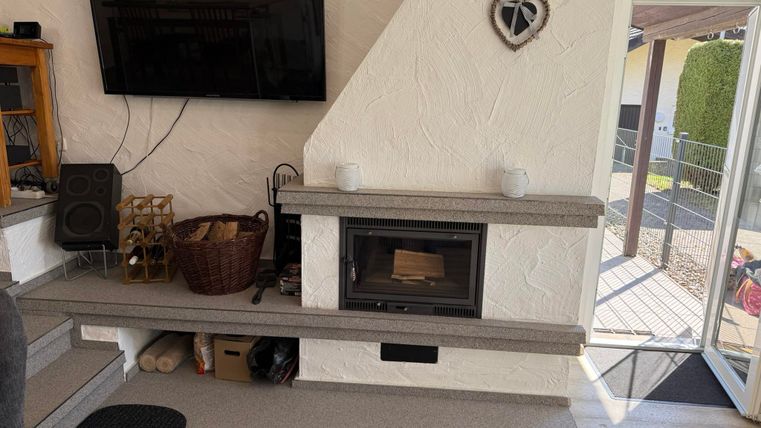 Un salon confortable avec une cheminée moderne et une grande télévision au mur. La pièce a des murs clairs et un accès à la terrasse.