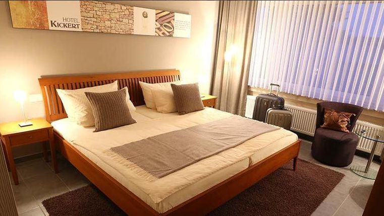 Une chambre confortable avec un grand lit double et des coussins doux. Les murs sont peints dans des couleurs claires et il y a un petit coin salon à côté de la fenêtre.