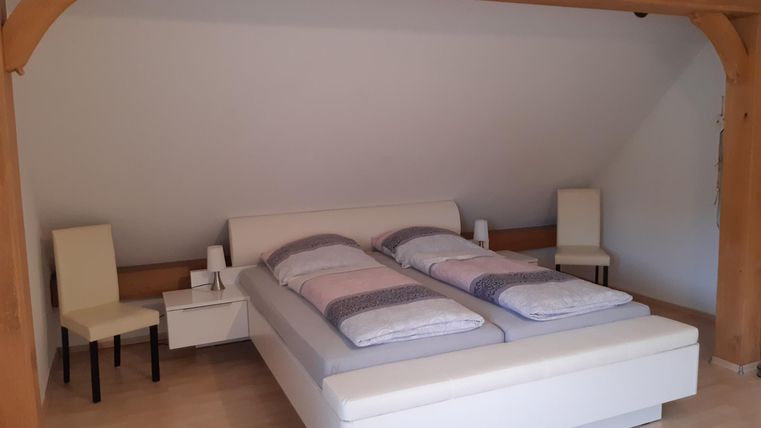 Een gezellige slaapkamer met een groot, wit bed. Naast het bed staan twee stoelen en nachtkastjes.