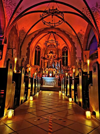 Ein schöner Kirchenraum mit warmem, orangefarbenem Licht. Der Altar ist gut sichtbar und von Kerzen umgeben.