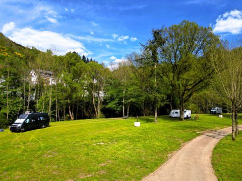 Ein ruhiger Campingplatz mit grüner Wiese und mehreren Wohnmobilen. Im Hintergrund sind Bäume und ein blauer Himmel zu sehen.