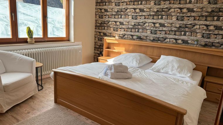 Ein gemütliches Schlafzimmer mit einem Doppelbett und frischen weißen Bettdecken. Das Zimmer hat große Fenster und eine schöne Steinwand.