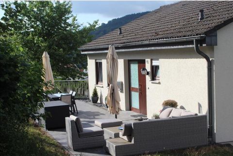 Eine moderne Terrasse mit bequemen Möbeln und Sonnenschirmen. Im Hintergrund steht ein helles Haus umgeben von Bäumen.