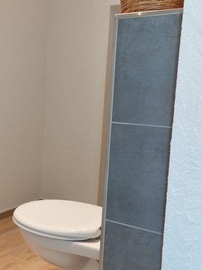 Een moderne badkamer met een wit toilet en een grijze tegels. Op de achtergrond is een wasmand te zien.