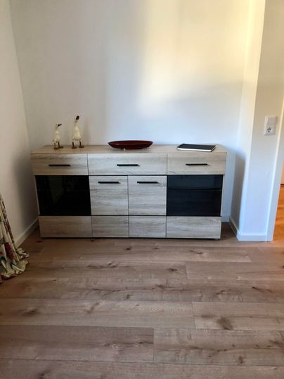 A modern sideboard made of wood with black elements. On it sits a decorative bowl and two small figurines.