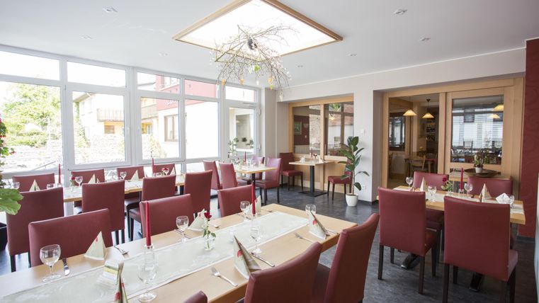 Ein elegantes Restaurant mit roten Stühlen und großen Fenstern. Der Tisch ist schön gedeckt und es gibt eine moderne Beleuchtung.