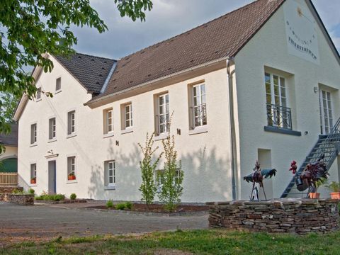 Een modern, licht gebouw met een witte façade en grote ramen. Aan de zijkant zijn enkele decoratieve figuren en een verzorgde buitenruimte te zien.