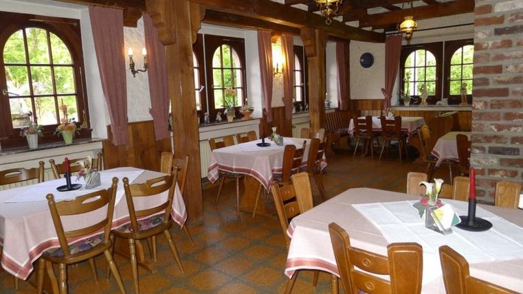 An inviting restaurant with wooden furniture and beautiful windows. The tables are decorated with white tablecloths and flowers.