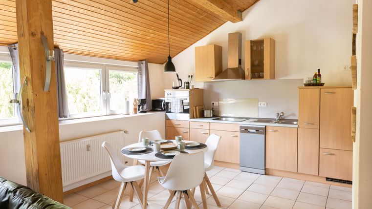 A modern kitchen with a dining table and chairs. Large windows provide plenty of light and a cozy atmosphere.