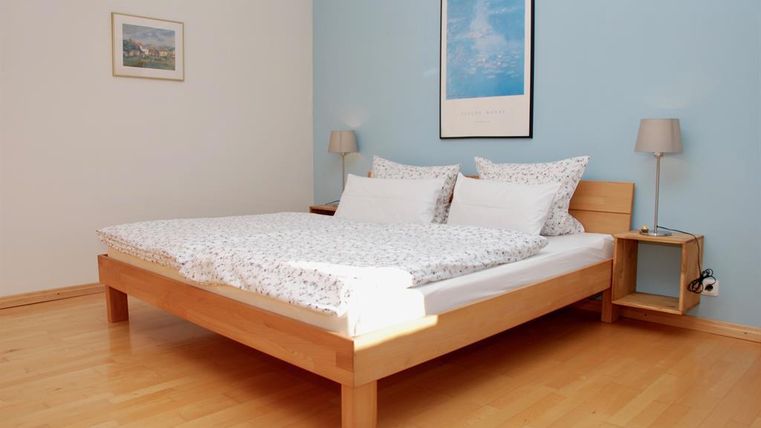 Ein gemütliches Schlafzimmer mit einem Holzbett und frischen Bettwäsche. Der Raum hat eine helle, freundliche Atmosphäre mit einer blauen Wand.