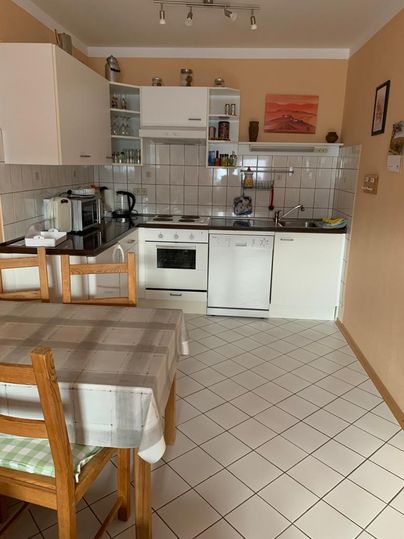 Een lichte keuken met moderne apparaten en een eetgroep. De muren zijn in een warme tint gehouden, en de tegels zijn neutraal.