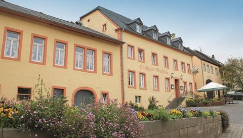 Ein historisches Gebäude mit einer gelben Fassade und roten Akzenten. Vor dem Gebäude blühen bunte Blumen und es gibt einen Außenbereich mit Tischen.
