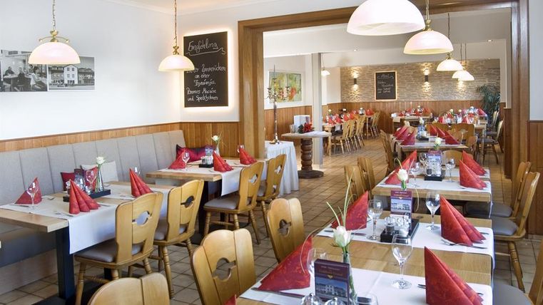 Een gezellig restaurant met houten meubels en mooi gedekte tafels. Rode stoffen servetten en een uitnodigende sfeer creëren een aangename ambiance.