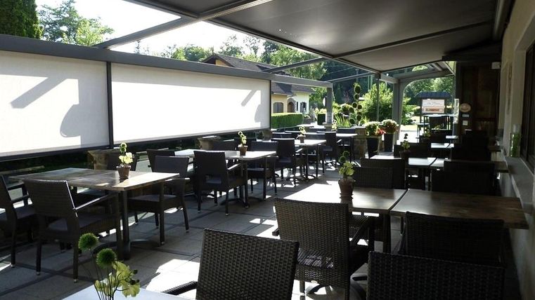 Een gezellige buitenruimte van een café met meerdere tafels en stoelen. Het terras is versierd met planten en heeft een heldere lucht op de achtergrond.