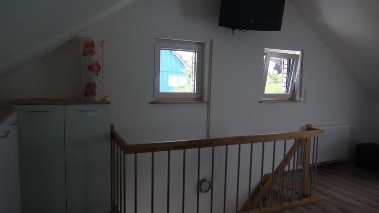 Une pièce confortable dans le grenier avec un petit garde-fou et des fenêtres. Un téléviseur est accroché au mur, et il y a une armoire ainsi qu'une vue sur les environs.