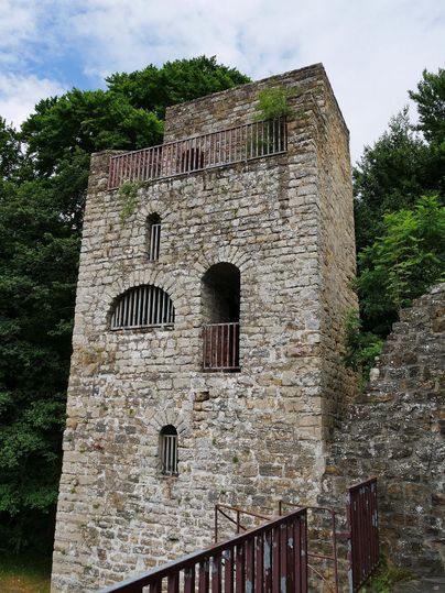 Ein historischer Steinturm umgeben von Bäumen. Einige Fenster sind mit Gitterstäben versehen.