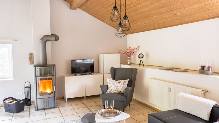 A cozy living room with a modern stove and wooden ceilings. Comfortable furniture and a table create an inviting atmosphere.