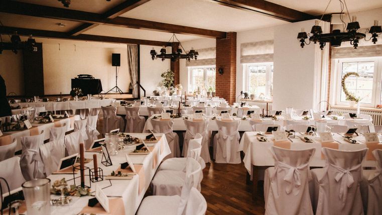 Une salle d'événement élégante avec des tables dressées de façon festive et des chaises blanches. L'atmosphère est accueillante et prête pour un événement spécial.
