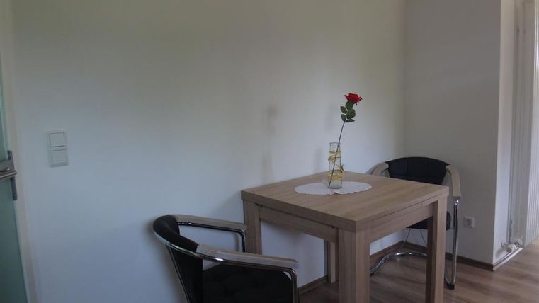 Une pièce lumineuse avec une table et deux chaises. Sur la table se trouve une rose dans un vase.