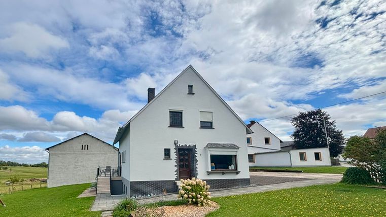 Ein modernes, weißes Haus mit einer gepflegten Umgebung. Der Himmel ist bewölkt und die Wiese ist grün.