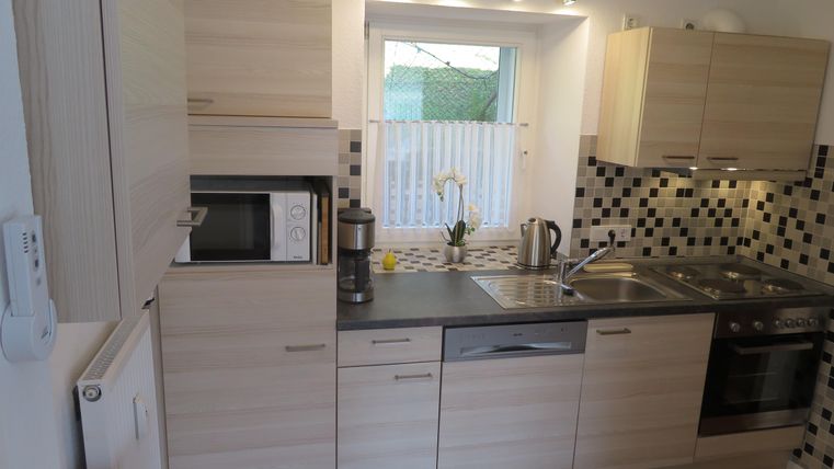 Een moderne keuken met lichte houten meubels en een elegante tegelachterwand. Ze is goed uitgerust met een kookplaat, een magnetron en een waterkoker.