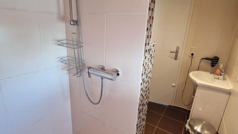 A modern shower with tiles and a hand wash basin. The room is bright and well-equipped.