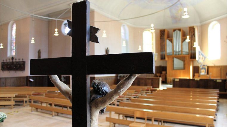 Une église silencieuse avec une statue en bois sur la croix au premier plan. À l'arrière-plan, des bancs et un orgue sont visibles.