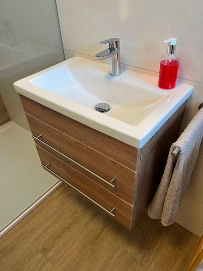 Un lavabo moderne avec un meuble en bois dans une salle de bains. À côté du lavabo se trouve un liquide rouge et une serviette pend à côté.