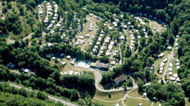 Een luchtfoto van een camping in een groene omgeving. De tent- en caravanplaatsen zijn netjes gerangschikt en omringd door bomen.