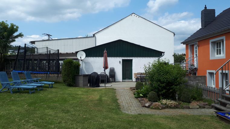 A quiet garden with a lawn area, sun loungers, and two buildings. The sky is blue with some clouds.