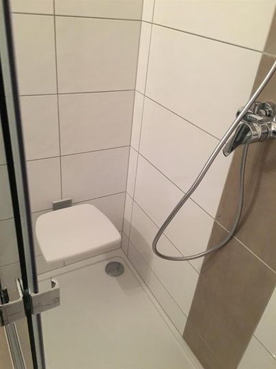 Une cabine de douche moderne avec des carreaux blancs. La douche est compacte et est équipée d'un pommeau de douche à main.