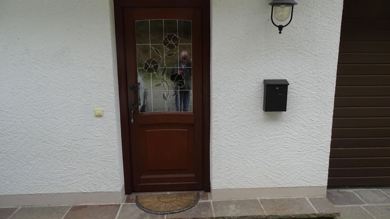 Une porte d'entrée marron avec des éléments en verre et une boîte aux lettres moderne. À côté de la porte, un appliqué mural est installé.