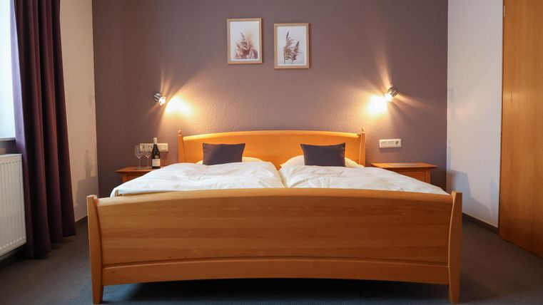 Une chambre confortable avec un lit double et deux coussins douillets. Des images sont accrochées aux murs, et il y a une lumière douce provenant des appliques murales.