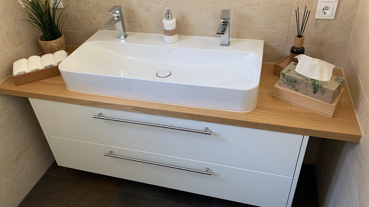 Een moderne badkamer met een elegant wastafel en houten werkblad. De inrichting is helder en stijlvol, met planten en decoraties.